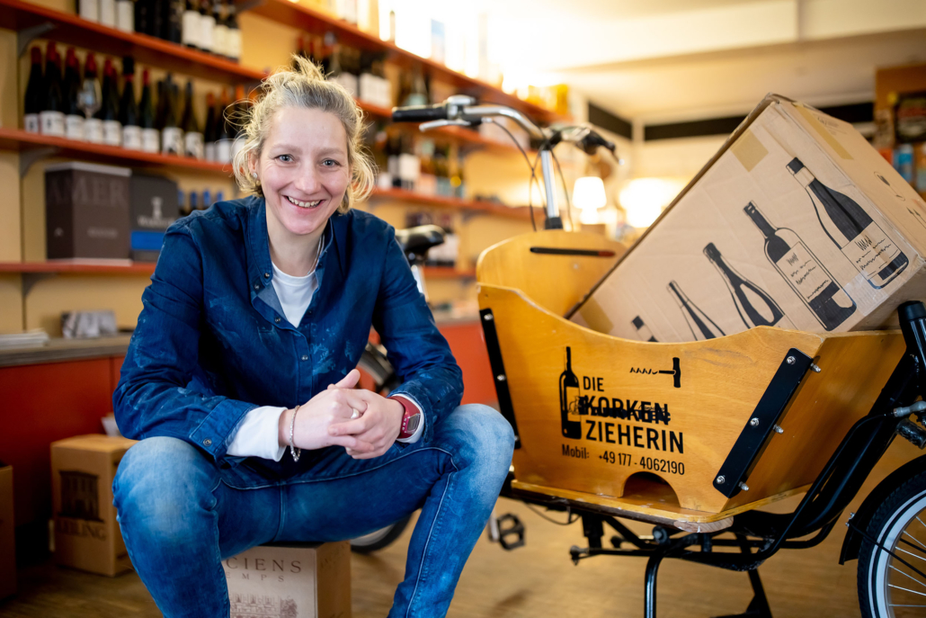 Portraitbild der Korkenzieherin Ornett Ragoschat mit dem Lastenfahrrad im Weingeschäft